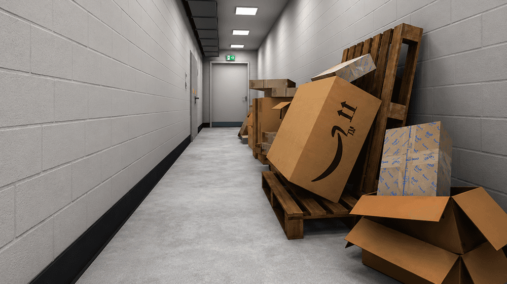 Un itinéraire d'évacuation dans un couloir est bloqué par des palettes et des cartons empilés contre le mur, une issue de secours illuminée au bout.